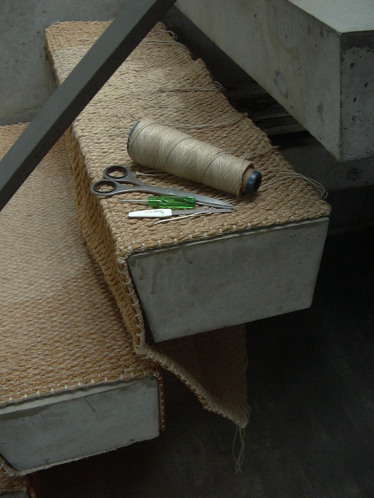 階段マットのすり減った部分に補修の糸を織り込み、階段に取り付ける作業を行っています