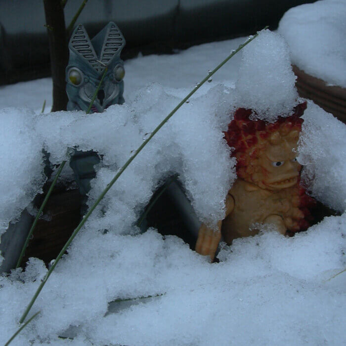 雪夏至の庭に佇むバルタン星人の人形とピグモンの人形