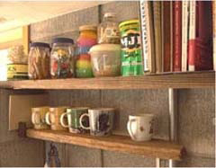 キッチンのこまごまな瓶やマグカップ、本が置かれた、庭にころがってた板で作った棚