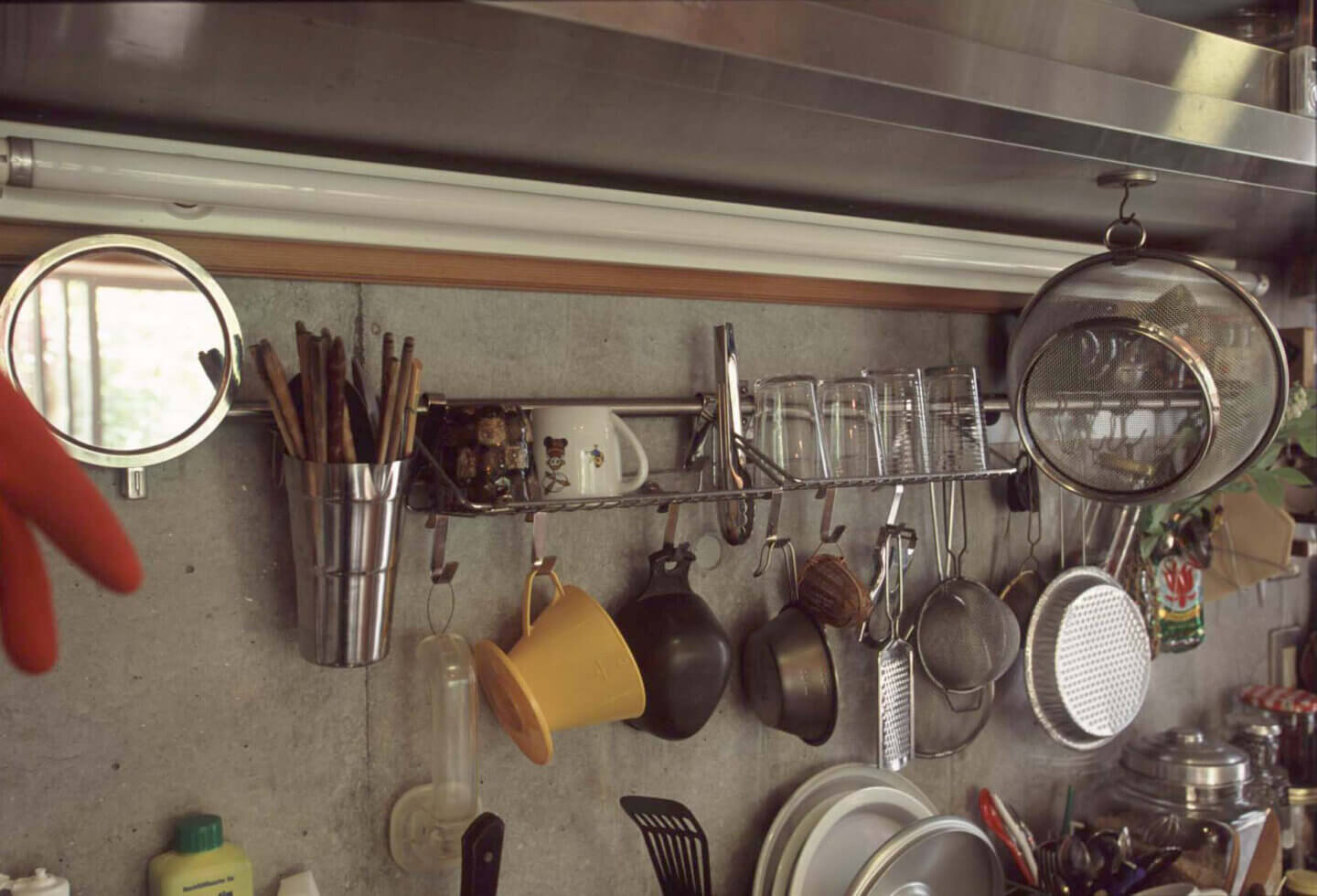 コンクリートのキッチンの壁にかけられた、リサイクル店で集めた、たくさんの業務用の調理器具