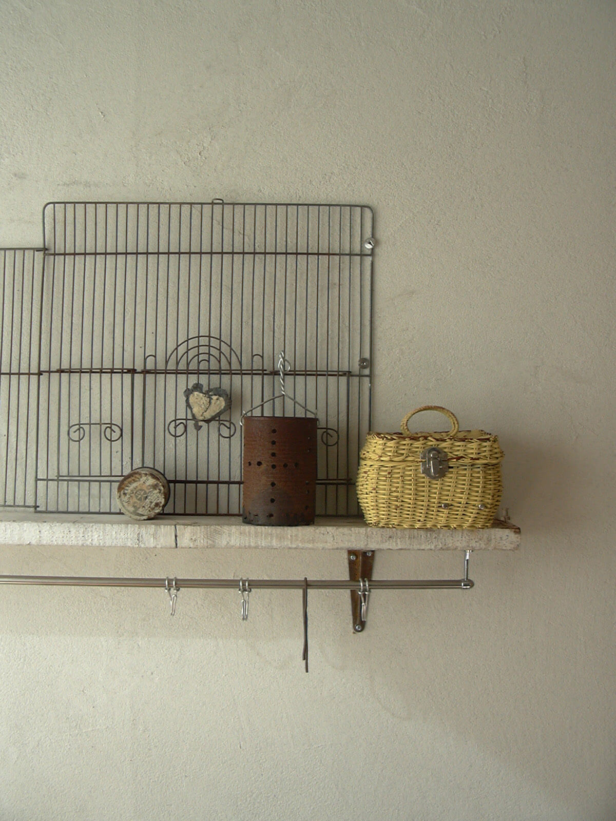 下には金属の棒にフックが掛けられ、上には鳥かごの網、籐のカゴ、金属の缶が置かれている白い壁に取り付けられた棚