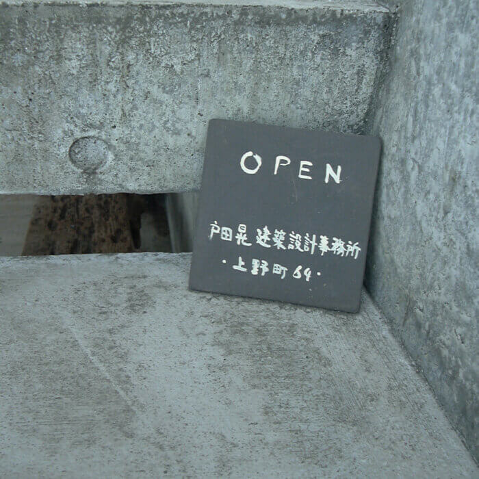 コンクリートの階段に置かれた、黒地に白字で書かれた戸田晃建築設計事務所の小さな看板