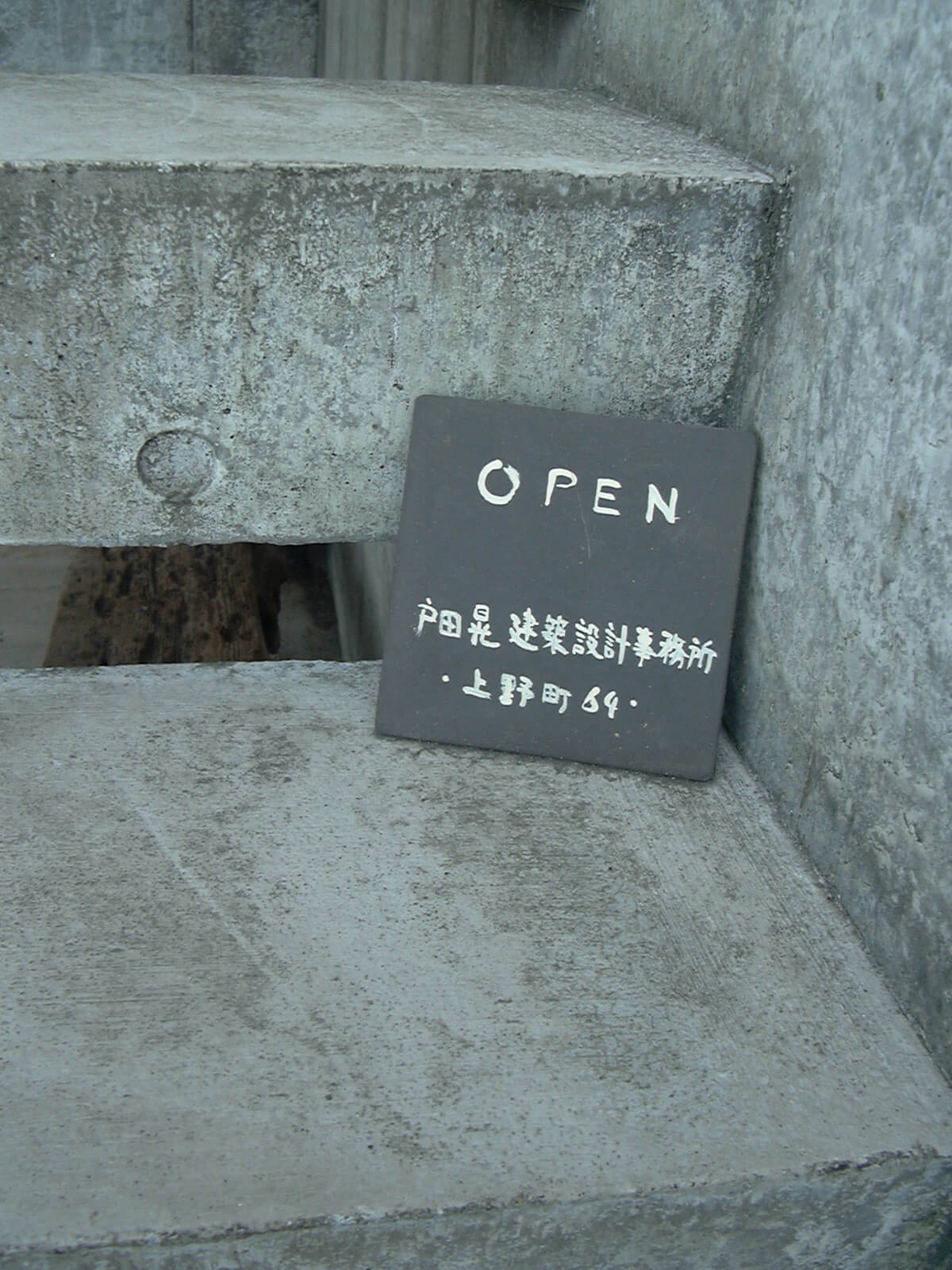 コンクリートの階段に置かれた、黒地に白字で書かれた戸田晃建築設計事務所の小さな看板