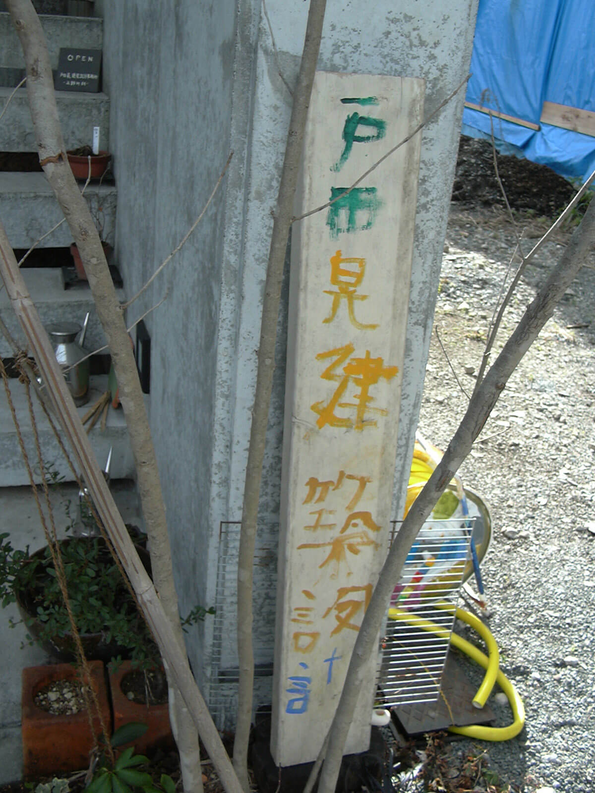コンクリートの壁に立てかけられた、細長い木に子供の字で書かれた、戸田晃建築設計事務所の看板