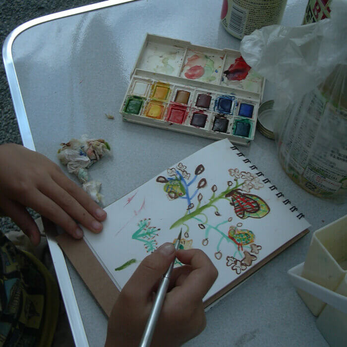 屋外のテーブルで、子どもが絵の具でイラストを描いている