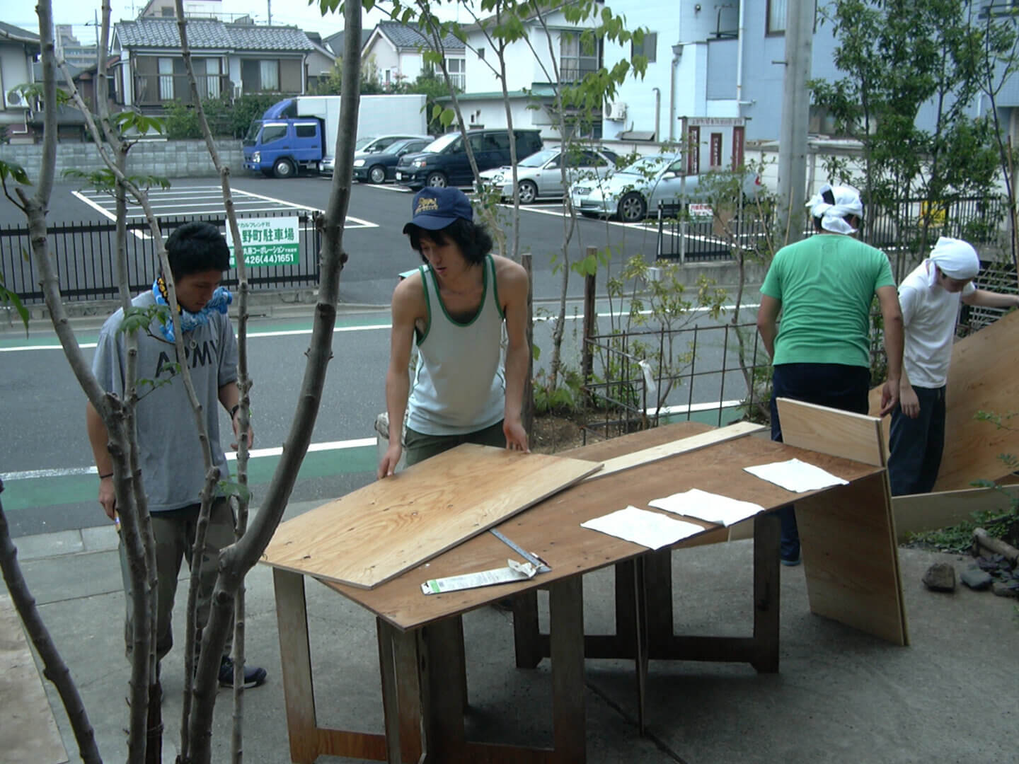 玄関先で小屋工事のための板を準備している、4人の若い男性