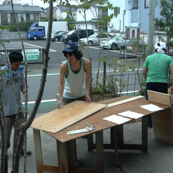 玄関先で小屋工事のための板を準備している、4人の若い男性