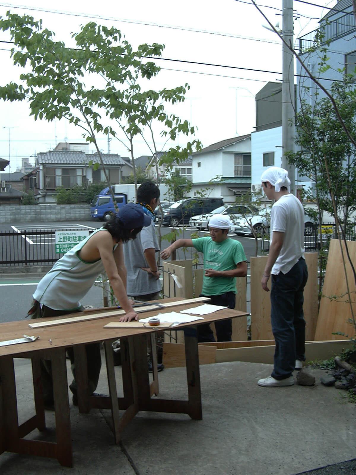 玄関先で木の板を見ながら小屋工事のための話し合いをしている、4人の若い男性