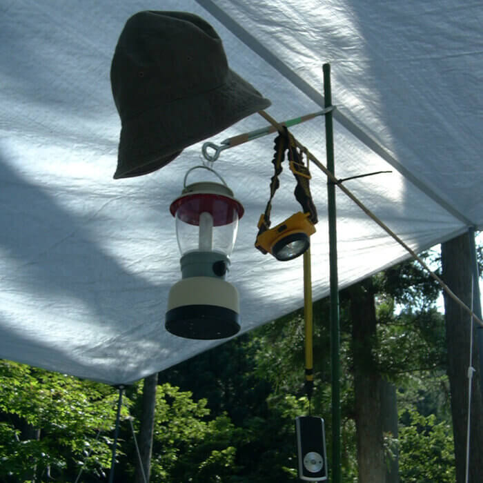 シート、棒、ロープとタープで立てたテントの中の柱に吊るされた、懐中電灯とランプ