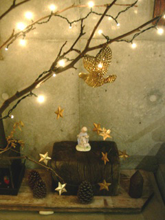 こげ茶の木片の上に乗った陶器の人形、まつぼっくり、ライトアップされた細い木の枝などのクリスマスの飾り