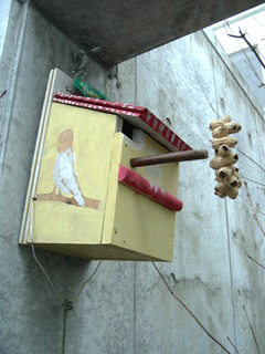 コンクリートの壁に掛けられた、手作りの木でできた黄色と赤の鳥小屋