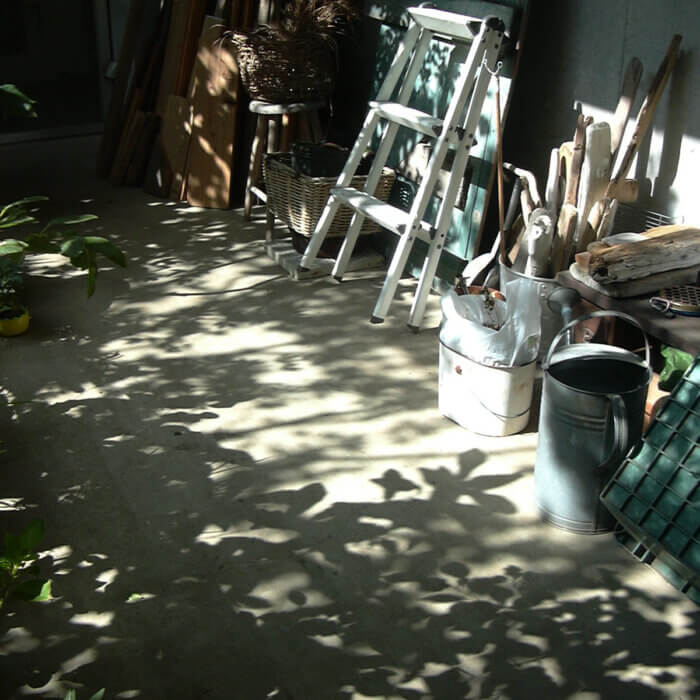 木の板や棒、脚立などが置いてある庭の、コンクリートの床に映っている9月の木の影
