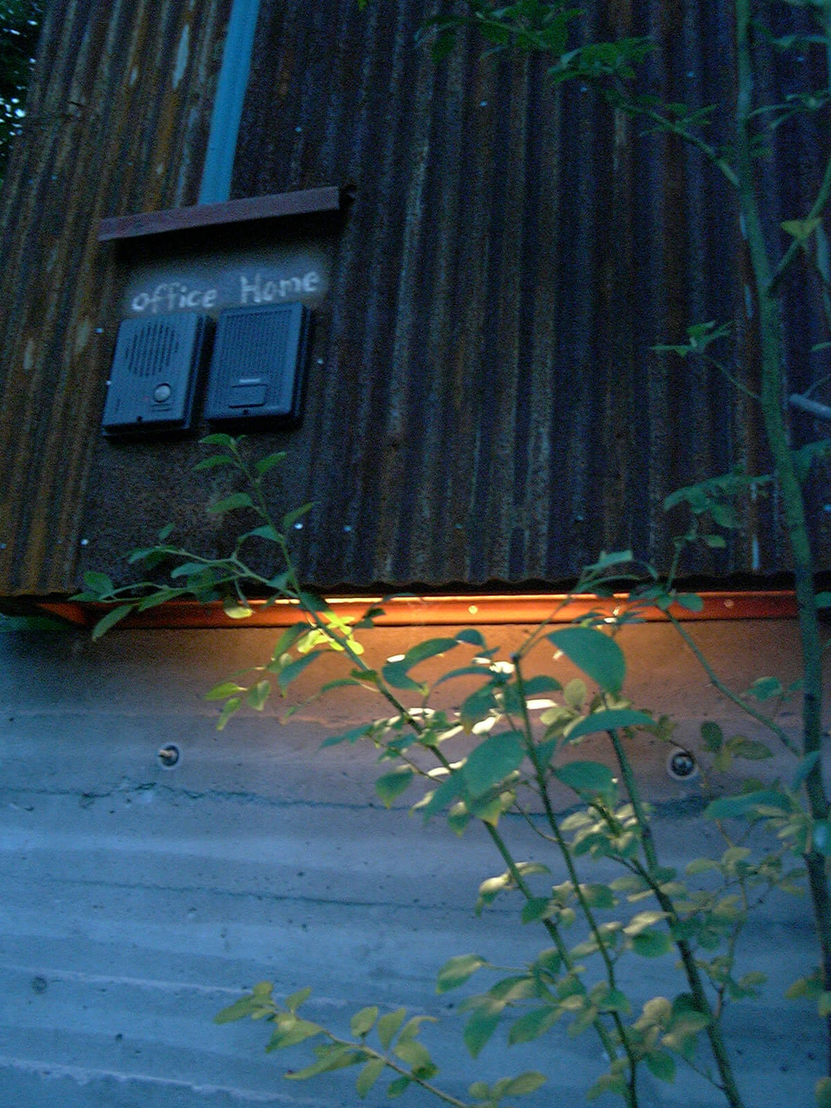 夕方の緑に囲まれた小屋の、壁のすき間から見える暖かい色のあかり