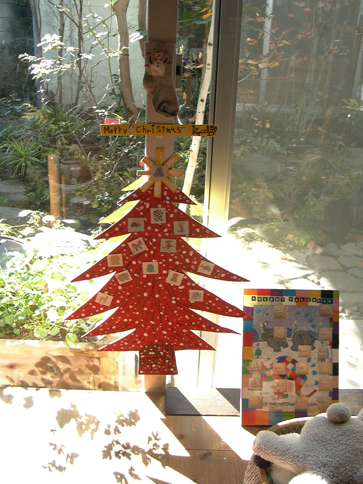 窓際に置かれた、アドベントカレンダーのふたの紙を貼り付けた、段ボールでできた赤いクリスマスツリー