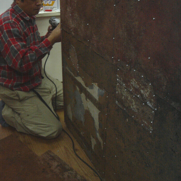 事務所の改装工事のため、大きな鉄の板を電動ドライバーで工事している男性