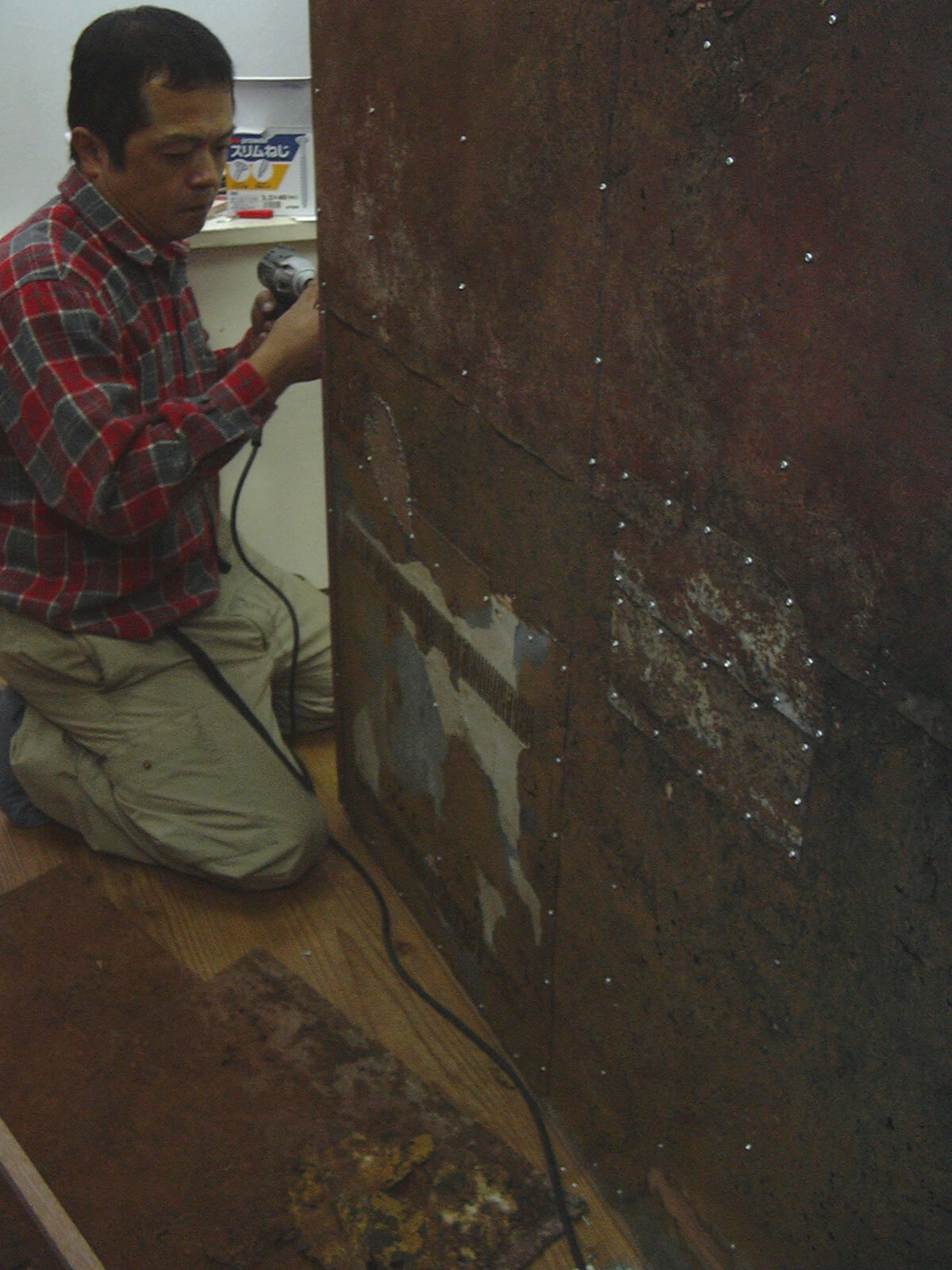 事務所の改装工事のため、大きな鉄の板を電動ドライバーで工事している男性